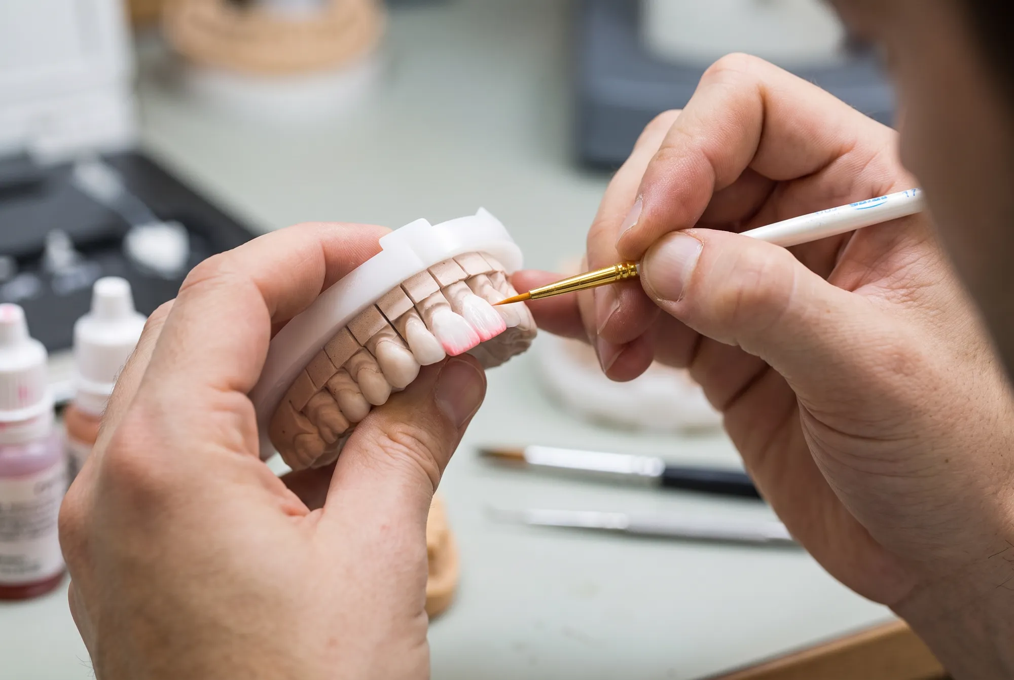 A ceramist hand-painting a porcelain dental restoration with a fine brush